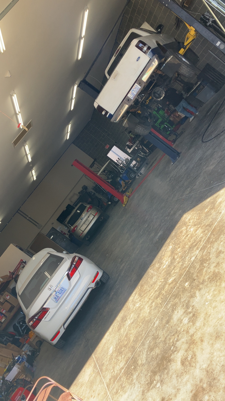 A photo of the garage at On Call Auto Care in Lexington North Carolina with cars being worked on and a white truck up on a car lift several feet off the ground